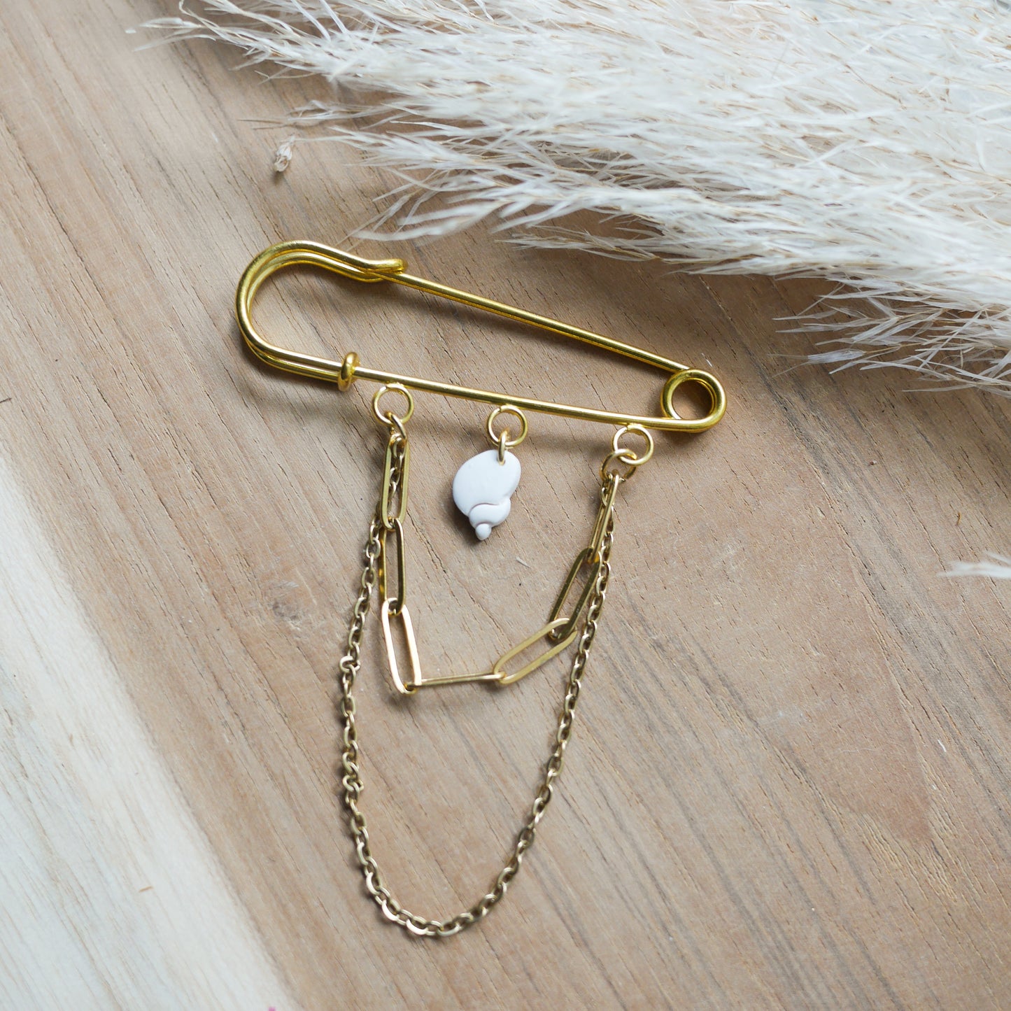Broche Malé avec chaînes dorées et coquillage blanc en pâte polymère.